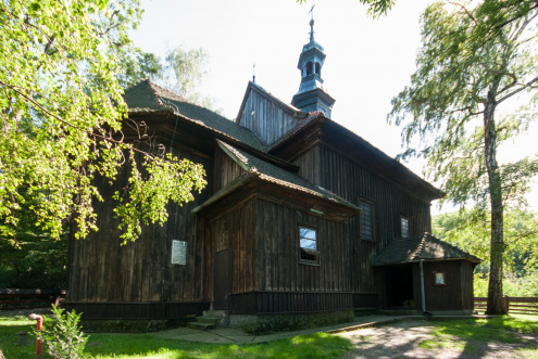 Widok drewnianego kościoła św. Sebastiana w Wieliczce pośród trzew i zieleni.