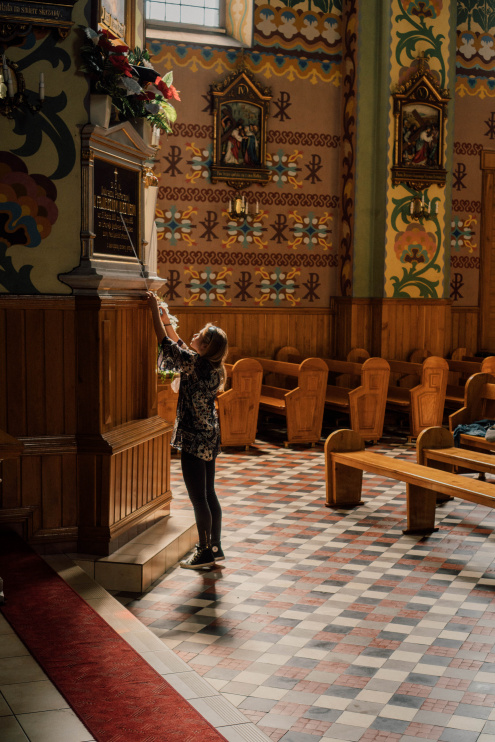 Scena w kościele. Inwentaryzatorka stoi przez wmurowaną w ścianę świątyni tablicą pamiątkową