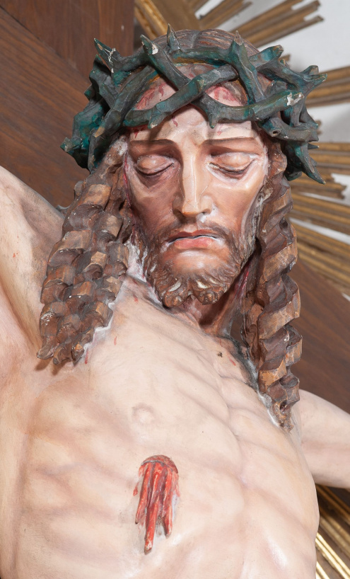 Fragment rzeźby „Chrystus Ukrzyżowany”, ukazujący głowę Chrystusa w koronie cierniowej bezwiednie opadającą na pierś, z widocznym przebitym, krwawiącym bokiem.