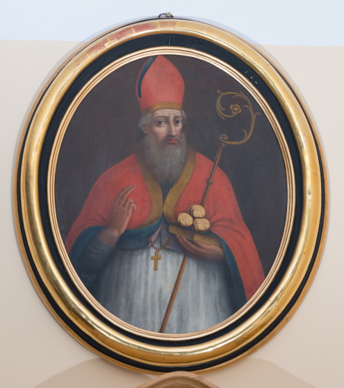 Obraz z wizerunkiem św. Mikołaja, ukazanego w półpostaci, jako starca, w stroju biskupim. Prawą dłonią błogosławi, lewą przytrzymuje pastorał i podtrzymuje księgę z trzema kulami.