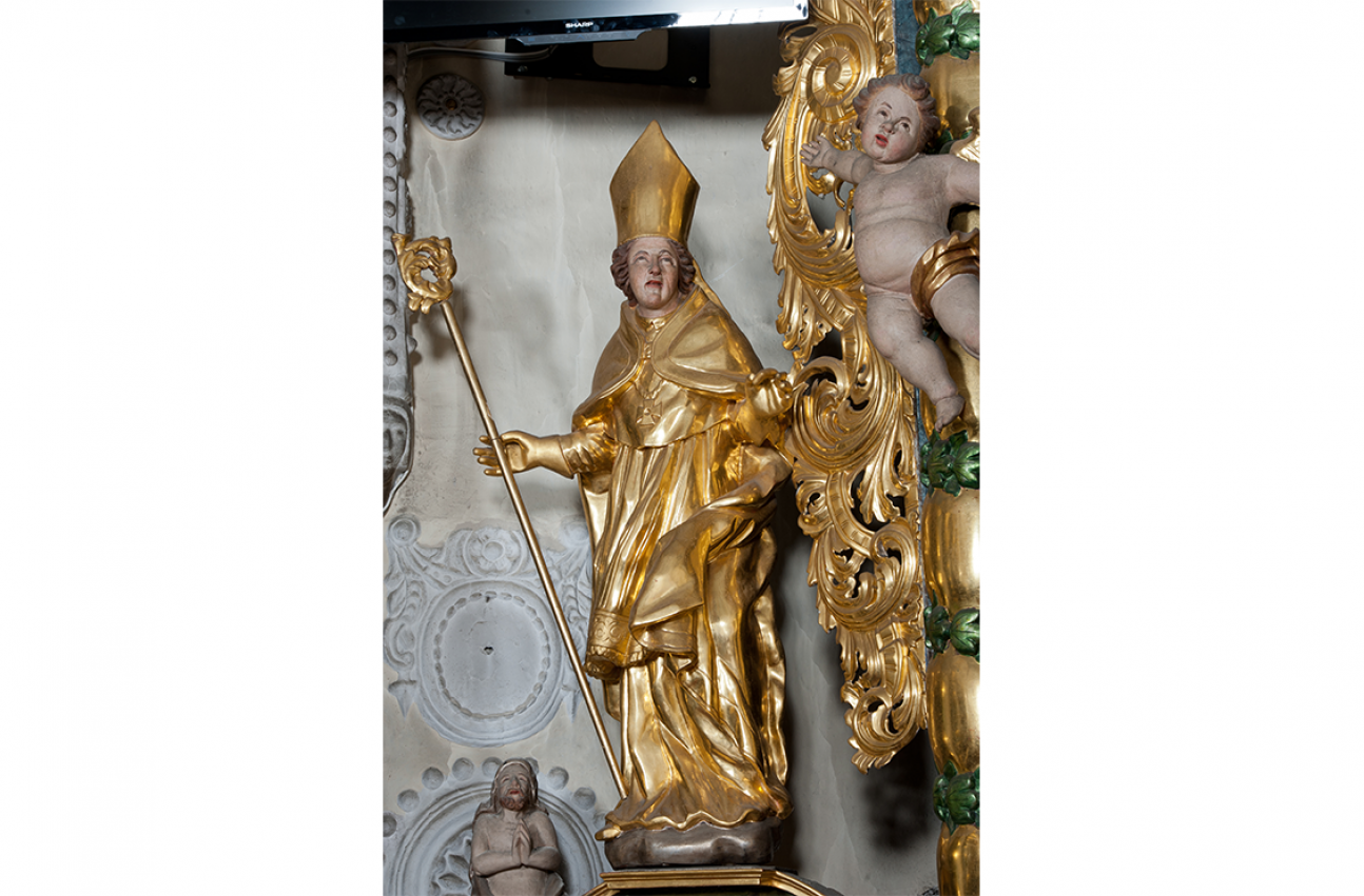 Rzeźba świętego Marcina we Frydmanie. Święty ukazany całopostaciowo. Ubrany jest w humerał, albę, rokietę, mucet, krzyż pektoralny, kapę, rękawiczki, infułę i pastorał.