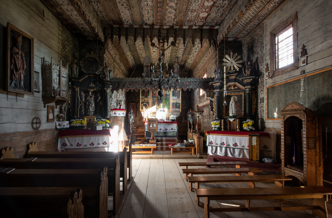 Zdjęcie 6. Wnętrze kościoła w Dębnie Podhalańskim. Na pierwszym planie widoczne  dwa rzędy ławek, w oddali ołtarz główny.