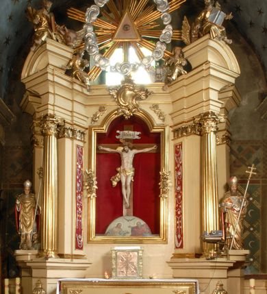 Zdjęcie nr 7: Drewniana, pełnoplastyczna, polichromowana figura Chrystusa Ukrzyżowanego w typie Christo vivo na drewnianym krzyżu znajduje się we wnęce części środkowej ołtarza głównego w kościele pw. Wszystkich Świętych w Babicach. Sylwetkę charakteryzuje wyrazista muskulatura ciała. Zwróconą w trzech czwartych w lewo głowę, lekko pochyloną w dół, charakteryzuje pociągła twarz o wyrazistych rysach, lekko przymkniętych oczach i z krótkim, rozdwojonym na końcu zarostem. Długie, brązowe, skręcone w pukle włosy opadają na plecy i prawe ramię. Głowę wieńczy złocona, cierniowa korona i okalają trzy wiązki złoconych promieni. Ramiona są w płytkim, T-kształtnym zwisie, klatka piersiowa z zaznaczoną linią żeber. Biodra osłania krótkie, złocone, przewiązane sznurem, mocno fałdowane perizonium z długim, rozwianym zwisem na prawym boku. Nogi przybite są jednym gwoździem. Na czole, torsie, rękach i stopach widoczne są strużki krwi. W górnej części pionowej belki krzyża znajduje się srebrzony titulus ze złoconym napisem: INRI. Wnęka przesłaniana jest zasuwą z przedstawieniem Wszystkich Świętych.         

  