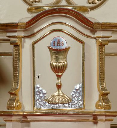 Zdjęcie nr 6: Ołtarz przyścienny, narożny, usytuowany po prawej stronie, w pierwszym od prezbiterium przęśle nawy, przy ścianie tęczowej. Architektoniczny, jednokondygnacyjny ze zwieńczeniem. Mensa murowana, prostopadłościenna, w typie skrzyniowym, z relikwiami nieznanego z imienia jednego ze świętych męczenników. Antepedium z blachy w drewnianej ramie, z monogramem imienia Jezus w centrum. Niewielkie, drewniane tabernakulum architektoniczne, na cokole. Jednoskrzydłowe drzwiczki zdobione płaskorzeźbionym kielichem z hostią, flankowane pilastrami o trzonach spływających wolutowo, podtrzymujących wyłamany gzyms. Nastawa ołtarzowa wsparta na flankujących mensę wysokich, dwudzielnych postumentach, dekorowanych złoconymi płycinami zdobionymi rocaille'em. Części boczne na całej wysokości ustawione ukośnie w stosunku do osi środkowej ołtarza. Wysunięte przed zdwojone pilastry z trzonami dekorowanymi rocaille'ami, kolumny o kanelowanych na całej wysokości, złoconych trzonach i kompozytowych kapitelach, dźwigają bogato profilowane, gierowane, pełne belkowanie, wyłamane na osi podpór. Wieńczy je przerwany, półkolisty przyczółek. W polu nastawy złocona, profilowana rama o kształcie stojącego, podciętego półkoliście u podstawy prostokąta zamkniętego łukiem wklęsło-wypukłym z uskokiem. Poniżej i powyżej złocone aplikacje w formie mocno przestylizowanych liści akantu i muszli palmetowych. Wewnątrz wysuwane dwa obrazy: z Matką Boską Różańcową w sukience i ze św. Anną (obecnie niedostępny – popsuty mechanizm wysuwający). Na belkowaniu osadzony rocaille'owy kartusz. Zwieńczenie o wykrojonych wolutowo bokach zamknięte łukiem wklęsło-wypukłym, utworzonym przez dwie przeciwstawne woluty. U szczytu złocona, ażurowo wycinana muszla palmetowa. W polu zwieńczenia obraz na płótnie ze św. Józefem i Dzieciątkiem w kształcie stojącego prostokąta o ściętych krawędziach dolnych i wklęsłych bokach, zamkniętego łukiem wklęsło-wypukłym z uskokiem. Flankują go dwie niewielkie aplikacje rocaille'owe. Na tylne postumenty cokołu spływają woluty, lewa z monogramem maryjnym. 
Ołtarz obecnie przemalowany na kremowo. Ornamenty, załamania profili, ramy, trzony kolumn są złocone.