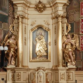 Zdjęcie nr 1: Ołtarz przyścienny, narożny, usytuowany po lewej stronie, w pierwszym od prezbiterium przęśle nawy, przy ścianie tęczowej. Architektoniczny, jednokondygnacyjny ze zwieńczeniem. Mensa murowana, prostopadłościenna, w typie skrzyniowym, z relikwiami nieznanego z imienia świętego męczennika. Antepedium z blachy w drewnianej ramie, z monogramem maryjnym w centrum. Niewielkie, drewniane tabernakulum jednodrzwiowe; lekko wypukłe drzwiczki zdobione płaskorzeźbionym kielichem z hostią wkomponowanym w złoconą płycinę zamkniętą łukiem nadwieszonym. Boki tabernakulum ujęte wolutowymi esownicami ustawionymi ukośnie w stosunku do jego lica. Zwieńczenie w formie przeciwstawnych wolut zdobionych rocaille'em. Nastawa ołtarzowa wsparta na flankujących mensę wysokich, dwudzielnych postumentach dekorowanych złoconymi płycinami zdobionymi rocaille'em. Części boczne na całej wysokości ustawione ukośnie w stosunku do osi środkowej ołtarza. Wysunięte przed zdwojone pilastry z trzonami dekorowanymi rocaille'ami, kolumny o kanelowanych na całej wysokości, złoconych trzonach i kompozytowych kapitelach, dźwigają bogato profilowane, gierowane, pełne belkowanie, wyłamane na osi podpór. Wieńczy je przerwany, półkolisty przyczółek. W polu nastawy złocona, profilowana rama o kształcie stojącego prostokąta zamkniętego łukiem wklęsło-wypukłym z uskokiem. Na jej boku, z prawej strony nałożona złocona aplikacja kwiatowa. Wewnątrz wysuwane dwa obrazy: z Matką Boską Niepokalanie Poczętą i Aniołem Stróżem (obecnie wyjęty) pędzla Wojciecha Eljasza-Radzikowskiego. Na belkowaniu osadzony rocaille'owy kartusz. Zwieńczenie o wykrojonych wolutowo bokach zamknięte łukiem wklęsło-wypukłym utworzonym przez dwie przeciwstawne woluty. U szczytu złocona, ażurowo wycinana, muszla palmetowa. W polu obraz na blasze ze św. Antonim Padewskim i Dzieciątkiem Jezus w kształcie stojącego prostokąta o ściętych krawędziach dolnych i wklęsłych bokach, zamkniętego łukiem wklęsło-wypukłym z uskokiem. Flankują go dwie, niewielkie aplikacje rocaille'owe. Na tylnych postumentach cokołu dwie dużych rozmiarów, pełnoplastyczne rzeźby aniołów. Postaci stojące w silnym kontrapoście, o tanecznych, dynamicznych pozach. Ciała muskularne, odziane w bogate, złocone, mocno fałdowane szaty. Skrzydła złocone, karnacje polichromowane. Po obu bokach ołtarza niewielkie uszy utworzone z rocaille'ów. Ołtarz obecnie przemalowany na kremowo. Ornamenty, załamania profili, ramy, trzony kolumn złocone.