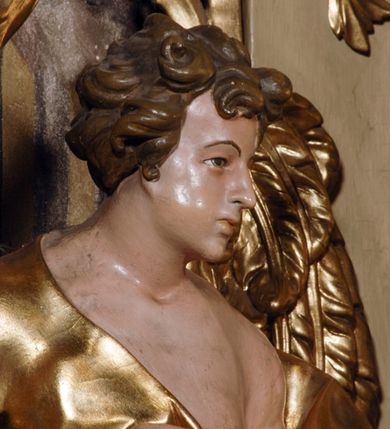 Zdjęcie nr 18: Ołtarz przyścienny, narożny, usytuowany po lewej stronie, w pierwszym od prezbiterium przęśle nawy, przy ścianie tęczowej. Architektoniczny, jednokondygnacyjny ze zwieńczeniem. Mensa murowana, prostopadłościenna, w typie skrzyniowym, z relikwiami nieznanego z imienia świętego męczennika. Antepedium z blachy w drewnianej ramie, z monogramem maryjnym w centrum. Niewielkie, drewniane tabernakulum jednodrzwiowe; lekko wypukłe drzwiczki zdobione płaskorzeźbionym kielichem z hostią wkomponowanym w złoconą płycinę zamkniętą łukiem nadwieszonym. Boki tabernakulum ujęte wolutowymi esownicami ustawionymi ukośnie w stosunku do jego lica. Zwieńczenie w formie przeciwstawnych wolut zdobionych rocaille&#039;em. Nastawa ołtarzowa wsparta na flankujących mensę wysokich, dwudzielnych postumentach dekorowanych złoconymi płycinami zdobionymi rocaille&#039;em. Części boczne na całej wysokości ustawione ukośnie w stosunku do osi środkowej ołtarza. Wysunięte przed zdwojone pilastry z trzonami dekorowanymi rocaille&#039;ami, kolumny o kanelowanych na całej wysokości, złoconych trzonach i kompozytowych kapitelach, dźwigają bogato profilowane, gierowane, pełne belkowanie, wyłamane na osi podpór. Wieńczy je przerwany, półkolisty przyczółek. W polu nastawy złocona, profilowana rama o kształcie stojącego prostokąta zamkniętego łukiem wklęsło-wypukłym z uskokiem. Na jej boku, z prawej strony nałożona złocona aplikacja kwiatowa. Wewnątrz wysuwane dwa obrazy: z Matką Boską Niepokalanie Poczętą i Aniołem Stróżem (obecnie wyjęty) pędzla Wojciecha Eljasza-Radzikowskiego. Na belkowaniu osadzony rocaille&#039;owy kartusz. Zwieńczenie o wykrojonych wolutowo bokach zamknięte łukiem wklęsło-wypukłym utworzonym przez dwie przeciwstawne woluty. U szczytu złocona, ażurowo wycinana, muszla palmetowa. W polu obraz na blasze ze św. Antonim Padewskim i Dzieciątkiem Jezus w kształcie stojącego prostokąta o ściętych krawędziach dolnych i wklęsłych bokach, zamkniętego łukiem wklęsło-wypukłym z uskokiem. Flankują go dwie, niewielkie aplikacje rocaille&#039;owe. Na tylnych postumentach cokołu dwie dużych rozmiarów, pełnoplastyczne rzeźby aniołów. Postaci stojące w silnym kontrapoście, o tanecznych, dynamicznych pozach. Ciała muskularne, odziane w bogate, złocone, mocno fałdowane szaty. Skrzydła złocone, karnacje polichromowane. Po obu bokach ołtarza niewielkie uszy utworzone z rocaille&#039;ów. Ołtarz obecnie przemalowany na kremowo. Ornamenty, załamania profili, ramy, trzony kolumn złocone.