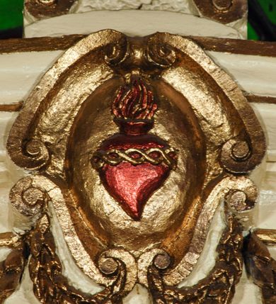 Zdjęcie nr 4: Ołtarz, architektoniczny, przyścienny, jednoosiowy, jednokondygnacyjny ze zwieńczeniem.  Mensa drewniana w postaci stołu wspartego na czterech nogach naśladujących w formie filary z impostowymi kapitelami. Retabulum posadowione na wysokim, dwudzielnym, rozczłonkowanym architektonicznie cokole, dekorowanym prostokątnymi płycinami o złoconych brzegach. Przednie ramiona cokołu ustawione ukośnie w stosunku do osi ołtarza. Na nich kolumny o kompozytowych kapitelach, wysunięte przed pilastry z pseudokorynckimi kapitelami i kanelurowanymi trzonami. Ujęte dołem parą wolut podpory dźwigają wyłamane ponad nimi, pełne belkowanie, przerwane na osi ołtarza. Na nim odcinki przyczółka w postaci wolut. Na architraw belkowania, ponad kapitelami kolumn nałożone pojedyncze liście akantu. Pomiędzy partiami przerwanego belkowania banderola rozpięta w formie półkolistego łuku, z napisem „ŚW(IĘTY) ANTONI MÓDL SIĘ ZA NAMI!". Pola odcinków przyczółka dekorowane złoconymi rocaille'ami. W polu ołtarza prostokątna nisza zamknięta łukiem koszowym z wydatnym kluczem w zwieńczeniu, ujęta złoconą, profilowaną ramą dekorowaną perełkowaniem. W niej pełnoplastyczna figura św. Antoniego Padewskiego. Wysokie, dużych rozmiarów trapezoidalne, ujęte po bokach motywem taśm zwieńczenie zamknięte fragmentem gzymsu w kształcie łuku odcinkowego, na osi którego kartusz wolutowy z motywem gorejącego serca pośrodku. Boki zwieńczenia w górnej partii ujęte parą wolut. Szczyt w formie krzyża na cokole z pary wolutek. W polu owalny obraz w złoconej, profilowanej ramie przedstawiający niezidentyfikowaną świętą. Wizerunek ujmują festony. Po bokach nastawy para figur św. Piotra i św. Pawła na wysuniętych partiach cokołu nastawy. Ołtarz w kolorze białym. Złocenia w partiach ornamentu oraz detalu architektonicznego.