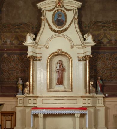 Zdjęcie nr 1: Ołtarz, architektoniczny, przyścienny, jednoosiowy, jednokondygnacyjny ze zwieńczeniem.  Mensa drewniana w postaci stołu wspartego na czterech nogach naśladujących w formie filary z impostowymi kapitelami. Retabulum posadowione na wysokim, dwudzielnym, rozczłonkowanym architektonicznie cokole, dekorowanym prostokątnymi płycinami o złoconych brzegach. Przednie ramiona cokołu ustawione ukośnie w stosunku do osi ołtarza. Na nich kolumny o kompozytowych kapitelach, wysunięte przed pilastry z pseudokorynckimi kapitelami i kanelurowanymi trzonami. Ujęte dołem parą wolut podpory dźwigają wyłamane ponad nimi, pełne belkowanie, przerwane na osi ołtarza. Na nim odcinki przyczółka w postaci wolut. Na architraw belkowania, ponad kapitelami kolumn nałożone pojedyncze liście akantu. Pomiędzy partiami przerwanego belkowania banderola rozpięta w formie półkolistego łuku, z napisem „ŚW(IĘTY) ANTONI MÓDL SIĘ ZA NAMI!". Pola odcinków przyczółka dekorowane złoconymi rocaille'ami. W polu ołtarza prostokątna nisza zamknięta łukiem koszowym z wydatnym kluczem w zwieńczeniu, ujęta złoconą, profilowaną ramą dekorowaną perełkowaniem. W niej pełnoplastyczna figura św. Antoniego Padewskiego. Wysokie, dużych rozmiarów trapezoidalne, ujęte po bokach motywem taśm zwieńczenie zamknięte fragmentem gzymsu w kształcie łuku odcinkowego, na osi którego kartusz wolutowy z motywem gorejącego serca pośrodku. Boki zwieńczenia w górnej partii ujęte parą wolut. Szczyt w formie krzyża na cokole z pary wolutek. W polu owalny obraz w złoconej, profilowanej ramie przedstawiający niezidentyfikowaną świętą. Wizerunek ujmują festony. Po bokach nastawy para figur św. Piotra i św. Pawła na wysuniętych partiach cokołu nastawy. Ołtarz w kolorze białym. Złocenia w partiach ornamentu oraz detalu architektonicznego.