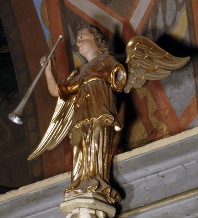 Zdjęcie nr 5: Ambona umieszczona na północnej ścianie, drugiego od prezbiterium przęsła nawy, przy lewym ramieniu transeptu. Ambona formie pięciobocznego kosza ze stożkowatą podstawą, zapleckiem i baldachimem zwieńczonym pełnoplastyczną rzeźbą archanioła dmącego w trąbę. Dostępna od wschodu – prowadzą do niej wysokie, trójdzielne schody z drewnianą balustradą. Dodatkowe drzwi znajdują się w ścianie północnej nawy, na prawo i nieco poniżej zaplecka. Stożkowata podstawa z polami dekorowanymi płaskorzeźbionymi, złoconymi rombami oddzielona od kosza za pomocą bogato profilowanego gzymsu. Kosz artykułowany za pomocą złoconych kolumienek na wolutowych postumentach, dźwigających odcinki niepełnego belkowania. W polach prostokątne płyciny o podciętych schodkowo podstawach zwieńczone łukiem nadwieszonym. W nich płaskorzeźbione przedstawienia od lewej: św. Jana z orłem piszącego piórem w księdze, stojącego na tle Golgoty, poniżej prostokątna tablica o ściętych narożach z napisem „Św(ięty) JAN”; św. Łukasza z piórem, kałamarzem i zamkniętą księgą w rękach, u jego stóp uskrzydlona głowa wołu, poniżej tablica z napisem „Św. ŁUKASZ”; Chrystusa siewcy ukazanego na tle pejzażu, poniżej tablica z monogramem „IHS”; św. Marka z księgą i piórem, uskrzydlony lew u jego stóp, poniżej tablica z napisem: „Św. MAREK”; św. Mateusza z piórem i księgą w ręku i klęczącym aniołem u jego stóp, poniżej tablica z napisem „Św(ięty) MATEUSZ”. Powyżej, w partiach fryzu analogiczne tablice z napisem „KTO JEST / Z BOGA / SŁÓW / BOŻYCH / SŁUCHA”. Kosz zwieńczony profilowanym gzymsem. Zaplecek ujęty pilastrami o kanelurowanych trzonach, w jego polu płycina w kształcie stojącego prostokąta o ściętych łukowato, wklęsłych narożach. W jej centrum płaskorzeźbione skrzyżowane tablice Dziesięciu Przykazań na srebrzonych obłokach, otoczone złoconymi promieniami. Baldachim czworoboczny zamknięty profilowanym gzymsem, pod którym podwieszona kotara z lambrekinem. Podniebie malowane na błękitny kolor z nałożoną w centrum, płaskorzeźbioną gołębicą Ducha Świętego w glorii. W zwieńczeniu ustawiona na wolutowym, rozczłonkowanym postumencie figura archanioła z trąbą. Rzeźba pełnoplastyczna, złocona, polichromowana. Postać wygięta łukowato, w prawej ręce wzniesionej ku górze trzyma długą trąbę. Lewej ręki brak. Anioł ubrany w długie, rozwiane, miękko układające się szaty przepasane sznurem. Twarz podłużna z wydatnymi policzkami, małym wystającym podbródkiem i dużymi, niebieskimi oczyma. Włosy sięgające ramion, kręcone, koloru brązowego.
Schody drewniane, trójdzielne z drewnianą balustradą zdobioną płycinami, w których nałożone, złocone aplikacje z silnie przestylizowanego akantu. Poręcz złocona zakończona niewielką wolutą.
Ambona malowana na kremowo, ze złoceniami w partiach ornamentów, załomach elementów architektonicznych oraz na szatach postaci.