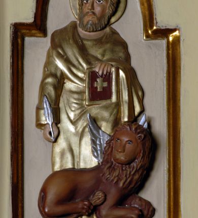 Zdjęcie nr 12: Ambona umieszczona na północnej ścianie, drugiego od prezbiterium przęsła nawy, przy lewym ramieniu transeptu. Ambona formie pięciobocznego kosza ze stożkowatą podstawą, zapleckiem i baldachimem zwieńczonym pełnoplastyczną rzeźbą archanioła dmącego w trąbę. Dostępna od wschodu – prowadzą do niej wysokie, trójdzielne schody z drewnianą balustradą. Dodatkowe drzwi znajdują się w ścianie północnej nawy, na prawo i nieco poniżej zaplecka. Stożkowata podstawa z polami dekorowanymi płaskorzeźbionymi, złoconymi rombami oddzielona od kosza za pomocą bogato profilowanego gzymsu. Kosz artykułowany za pomocą złoconych kolumienek na wolutowych postumentach, dźwigających odcinki niepełnego belkowania. W polach prostokątne płyciny o podciętych schodkowo podstawach zwieńczone łukiem nadwieszonym. W nich płaskorzeźbione przedstawienia od lewej: św. Jana z orłem piszącego piórem w księdze, stojącego na tle Golgoty, poniżej prostokątna tablica o ściętych narożach z napisem „Św(ięty) JAN”; św. Łukasza z piórem, kałamarzem i zamkniętą księgą w rękach, u jego stóp uskrzydlona głowa wołu, poniżej tablica z napisem „Św. ŁUKASZ”; Chrystusa siewcy ukazanego na tle pejzażu, poniżej tablica z monogramem „IHS”; św. Marka z księgą i piórem, uskrzydlony lew u jego stóp, poniżej tablica z napisem: „Św. MAREK”; św. Mateusza z piórem i księgą w ręku i klęczącym aniołem u jego stóp, poniżej tablica z napisem „Św(ięty) MATEUSZ”. Powyżej, w partiach fryzu analogiczne tablice z napisem „KTO JEST / Z BOGA / SŁÓW / BOŻYCH / SŁUCHA”. Kosz zwieńczony profilowanym gzymsem. Zaplecek ujęty pilastrami o kanelurowanych trzonach, w jego polu płycina w kształcie stojącego prostokąta o ściętych łukowato, wklęsłych narożach. W jej centrum płaskorzeźbione skrzyżowane tablice Dziesięciu Przykazań na srebrzonych obłokach, otoczone złoconymi promieniami. Baldachim czworoboczny zamknięty profilowanym gzymsem, pod którym podwieszona kotara z lambrekinem. Podniebie malowane na błękitny kolor z nałożoną w centrum, płaskorzeźbioną gołębicą Ducha Świętego w glorii. W zwieńczeniu ustawiona na wolutowym, rozczłonkowanym postumencie figura archanioła z trąbą. Rzeźba pełnoplastyczna, złocona, polichromowana. Postać wygięta łukowato, w prawej ręce wzniesionej ku górze trzyma długą trąbę. Lewej ręki brak. Anioł ubrany w długie, rozwiane, miękko układające się szaty przepasane sznurem. Twarz podłużna z wydatnymi policzkami, małym wystającym podbródkiem i dużymi, niebieskimi oczyma. Włosy sięgające ramion, kręcone, koloru brązowego.
Schody drewniane, trójdzielne z drewnianą balustradą zdobioną płycinami, w których nałożone, złocone aplikacje z silnie przestylizowanego akantu. Poręcz złocona zakończona niewielką wolutą.
Ambona malowana na kremowo, ze złoceniami w partiach ornamentów, załomach elementów architektonicznych oraz na szatach postaci.