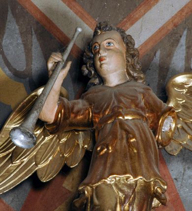 Zdjęcie nr 6: Ambona umieszczona na północnej ścianie, drugiego od prezbiterium przęsła nawy, przy lewym ramieniu transeptu. Ambona formie pięciobocznego kosza ze stożkowatą podstawą, zapleckiem i baldachimem zwieńczonym pełnoplastyczną rzeźbą archanioła dmącego w trąbę. Dostępna od wschodu – prowadzą do niej wysokie, trójdzielne schody z drewnianą balustradą. Dodatkowe drzwi znajdują się w ścianie północnej nawy, na prawo i nieco poniżej zaplecka. Stożkowata podstawa z polami dekorowanymi płaskorzeźbionymi, złoconymi rombami oddzielona od kosza za pomocą bogato profilowanego gzymsu. Kosz artykułowany za pomocą złoconych kolumienek na wolutowych postumentach, dźwigających odcinki niepełnego belkowania. W polach prostokątne płyciny o podciętych schodkowo podstawach zwieńczone łukiem nadwieszonym. W nich płaskorzeźbione przedstawienia od lewej: św. Jana z orłem piszącego piórem w księdze, stojącego na tle Golgoty, poniżej prostokątna tablica o ściętych narożach z napisem „Św(ięty) JAN”; św. Łukasza z piórem, kałamarzem i zamkniętą księgą w rękach, u jego stóp uskrzydlona głowa wołu, poniżej tablica z napisem „Św. ŁUKASZ”; Chrystusa siewcy ukazanego na tle pejzażu, poniżej tablica z monogramem „IHS”; św. Marka z księgą i piórem, uskrzydlony lew u jego stóp, poniżej tablica z napisem: „Św. MAREK”; św. Mateusza z piórem i księgą w ręku i klęczącym aniołem u jego stóp, poniżej tablica z napisem „Św(ięty) MATEUSZ”. Powyżej, w partiach fryzu analogiczne tablice z napisem „KTO JEST / Z BOGA / SŁÓW / BOŻYCH / SŁUCHA”. Kosz zwieńczony profilowanym gzymsem. Zaplecek ujęty pilastrami o kanelurowanych trzonach, w jego polu płycina w kształcie stojącego prostokąta o ściętych łukowato, wklęsłych narożach. W jej centrum płaskorzeźbione skrzyżowane tablice Dziesięciu Przykazań na srebrzonych obłokach, otoczone złoconymi promieniami. Baldachim czworoboczny zamknięty profilowanym gzymsem, pod którym podwieszona kotara z lambrekinem. Podniebie malowane na błękitny kolor z nałożoną w centrum, płaskorzeźbioną gołębicą Ducha Świętego w glorii. W zwieńczeniu ustawiona na wolutowym, rozczłonkowanym postumencie figura archanioła z trąbą. Rzeźba pełnoplastyczna, złocona, polichromowana. Postać wygięta łukowato, w prawej ręce wzniesionej ku górze trzyma długą trąbę. Lewej ręki brak. Anioł ubrany w długie, rozwiane, miękko układające się szaty przepasane sznurem. Twarz podłużna z wydatnymi policzkami, małym wystającym podbródkiem i dużymi, niebieskimi oczyma. Włosy sięgające ramion, kręcone, koloru brązowego.
Schody drewniane, trójdzielne z drewnianą balustradą zdobioną płycinami, w których nałożone, złocone aplikacje z silnie przestylizowanego akantu. Poręcz złocona zakończona niewielką wolutą.
Ambona malowana na kremowo, ze złoceniami w partiach ornamentów, załomach elementów architektonicznych oraz na szatach postaci.