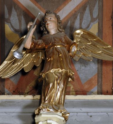 Zdjęcie nr 4: Ambona umieszczona na północnej ścianie, drugiego od prezbiterium przęsła nawy, przy lewym ramieniu transeptu. Ambona formie pięciobocznego kosza ze stożkowatą podstawą, zapleckiem i baldachimem zwieńczonym pełnoplastyczną rzeźbą archanioła dmącego w trąbę. Dostępna od wschodu – prowadzą do niej wysokie, trójdzielne schody z drewnianą balustradą. Dodatkowe drzwi znajdują się w ścianie północnej nawy, na prawo i nieco poniżej zaplecka. Stożkowata podstawa z polami dekorowanymi płaskorzeźbionymi, złoconymi rombami oddzielona od kosza za pomocą bogato profilowanego gzymsu. Kosz artykułowany za pomocą złoconych kolumienek na wolutowych postumentach, dźwigających odcinki niepełnego belkowania. W polach prostokątne płyciny o podciętych schodkowo podstawach zwieńczone łukiem nadwieszonym. W nich płaskorzeźbione przedstawienia od lewej: św. Jana z orłem piszącego piórem w księdze, stojącego na tle Golgoty, poniżej prostokątna tablica o ściętych narożach z napisem „Św(ięty) JAN”; św. Łukasza z piórem, kałamarzem i zamkniętą księgą w rękach, u jego stóp uskrzydlona głowa wołu, poniżej tablica z napisem „Św. ŁUKASZ”; Chrystusa siewcy ukazanego na tle pejzażu, poniżej tablica z monogramem „IHS”; św. Marka z księgą i piórem, uskrzydlony lew u jego stóp, poniżej tablica z napisem: „Św. MAREK”; św. Mateusza z piórem i księgą w ręku i klęczącym aniołem u jego stóp, poniżej tablica z napisem „Św(ięty) MATEUSZ”. Powyżej, w partiach fryzu analogiczne tablice z napisem „KTO JEST / Z BOGA / SŁÓW / BOŻYCH / SŁUCHA”. Kosz zwieńczony profilowanym gzymsem. Zaplecek ujęty pilastrami o kanelurowanych trzonach, w jego polu płycina w kształcie stojącego prostokąta o ściętych łukowato, wklęsłych narożach. W jej centrum płaskorzeźbione skrzyżowane tablice Dziesięciu Przykazań na srebrzonych obłokach, otoczone złoconymi promieniami. Baldachim czworoboczny zamknięty profilowanym gzymsem, pod którym podwieszona kotara z lambrekinem. Podniebie malowane na błękitny kolor z nałożoną w centrum, płaskorzeźbioną gołębicą Ducha Świętego w glorii. W zwieńczeniu ustawiona na wolutowym, rozczłonkowanym postumencie figura archanioła z trąbą. Rzeźba pełnoplastyczna, złocona, polichromowana. Postać wygięta łukowato, w prawej ręce wzniesionej ku górze trzyma długą trąbę. Lewej ręki brak. Anioł ubrany w długie, rozwiane, miękko układające się szaty przepasane sznurem. Twarz podłużna z wydatnymi policzkami, małym wystającym podbródkiem i dużymi, niebieskimi oczyma. Włosy sięgające ramion, kręcone, koloru brązowego.
Schody drewniane, trójdzielne z drewnianą balustradą zdobioną płycinami, w których nałożone, złocone aplikacje z silnie przestylizowanego akantu. Poręcz złocona zakończona niewielką wolutą.
Ambona malowana na kremowo, ze złoceniami w partiach ornamentów, załomach elementów architektonicznych oraz na szatach postaci.