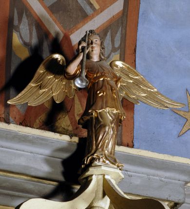 Zdjęcie nr 3: Ambona umieszczona na północnej ścianie, drugiego od prezbiterium przęsła nawy, przy lewym ramieniu transeptu. Ambona formie pięciobocznego kosza ze stożkowatą podstawą, zapleckiem i baldachimem zwieńczonym pełnoplastyczną rzeźbą archanioła dmącego w trąbę. Dostępna od wschodu – prowadzą do niej wysokie, trójdzielne schody z drewnianą balustradą. Dodatkowe drzwi znajdują się w ścianie północnej nawy, na prawo i nieco poniżej zaplecka. Stożkowata podstawa z polami dekorowanymi płaskorzeźbionymi, złoconymi rombami oddzielona od kosza za pomocą bogato profilowanego gzymsu. Kosz artykułowany za pomocą złoconych kolumienek na wolutowych postumentach, dźwigających odcinki niepełnego belkowania. W polach prostokątne płyciny o podciętych schodkowo podstawach zwieńczone łukiem nadwieszonym. W nich płaskorzeźbione przedstawienia od lewej: św. Jana z orłem piszącego piórem w księdze, stojącego na tle Golgoty, poniżej prostokątna tablica o ściętych narożach z napisem „Św(ięty) JAN”; św. Łukasza z piórem, kałamarzem i zamkniętą księgą w rękach, u jego stóp uskrzydlona głowa wołu, poniżej tablica z napisem „Św. ŁUKASZ”; Chrystusa siewcy ukazanego na tle pejzażu, poniżej tablica z monogramem „IHS”; św. Marka z księgą i piórem, uskrzydlony lew u jego stóp, poniżej tablica z napisem: „Św. MAREK”; św. Mateusza z piórem i księgą w ręku i klęczącym aniołem u jego stóp, poniżej tablica z napisem „Św(ięty) MATEUSZ”. Powyżej, w partiach fryzu analogiczne tablice z napisem „KTO JEST / Z BOGA / SŁÓW / BOŻYCH / SŁUCHA”. Kosz zwieńczony profilowanym gzymsem. Zaplecek ujęty pilastrami o kanelurowanych trzonach, w jego polu płycina w kształcie stojącego prostokąta o ściętych łukowato, wklęsłych narożach. W jej centrum płaskorzeźbione skrzyżowane tablice Dziesięciu Przykazań na srebrzonych obłokach, otoczone złoconymi promieniami. Baldachim czworoboczny zamknięty profilowanym gzymsem, pod którym podwieszona kotara z lambrekinem. Podniebie malowane na błękitny kolor z nałożoną w centrum, płaskorzeźbioną gołębicą Ducha Świętego w glorii. W zwieńczeniu ustawiona na wolutowym, rozczłonkowanym postumencie figura archanioła z trąbą. Rzeźba pełnoplastyczna, złocona, polichromowana. Postać wygięta łukowato, w prawej ręce wzniesionej ku górze trzyma długą trąbę. Lewej ręki brak. Anioł ubrany w długie, rozwiane, miękko układające się szaty przepasane sznurem. Twarz podłużna z wydatnymi policzkami, małym wystającym podbródkiem i dużymi, niebieskimi oczyma. Włosy sięgające ramion, kręcone, koloru brązowego.
Schody drewniane, trójdzielne z drewnianą balustradą zdobioną płycinami, w których nałożone, złocone aplikacje z silnie przestylizowanego akantu. Poręcz złocona zakończona niewielką wolutą.
Ambona malowana na kremowo, ze złoceniami w partiach ornamentów, załomach elementów architektonicznych oraz na szatach postaci.