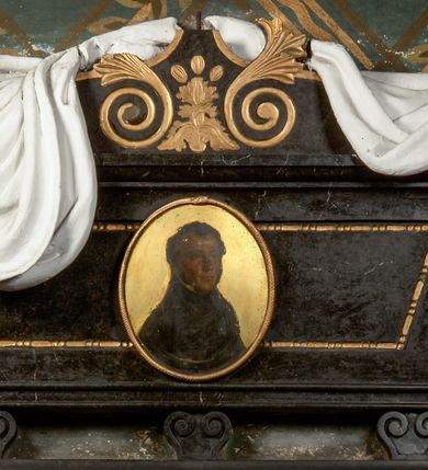 Zdjęcie nr 2: Rozbudowane epitafium utworzone z wysokiego cokołu z inskrypcją i wspartego na nim sarkofagu nakrytego tkaniną z portretem. Sarkofag stoi na trzech niewielkich nóżkach, zdobionych podwójnymi ustawionymi przeciwstawnie wolutami. Ma kształt równoramiennego trapezu, z dekorowaną perełkowaniem płyciną pośrodku i osadzonym w jej centrum, malowanym na owalnej, złoconej blasze portretem zmarłego. Zwieńczenie w kształcie łuku wklęsło-wypukłego, dekorowane złoconymi wolutami zakończonymi liśćmi akantu liściastymi wolutami w funkcji akroterionów oraz narzuconą nań, udrapowaną, białą tkaniną. Pośrodku owalny obraz w złoconej ramie naśladującej węża pożerającego własny ogon. Zmarły przedstawiony w popiersiu, z ciałem w trzech czwartych zwróconym w lewo. Ubrany w ciemny strój z wysokim kołnierzem. Tło jednolicie złocone. Na cokole, wspartym na dwóch piramidalnych konsolach ryta i złocona inskrypcja "FRANCISZKOWI ŁĄCKIEMU / KTÓRY DO ZASŁUG, I CNÓT OBYWATELSKICH, / ŁĄCZYŁ DOBROCZYNNOŚĆ. / A TEY BŁOGI WPŁYW DOSIĘGNĄŁ WIELU. / W WIEKU LAT 54 D(NIA) 15 WRZEŚNIA 1844. R(OKU) ZMARŁEMU."