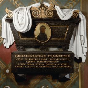 Zdjęcie nr 1: Rozbudowane epitafium utworzone z wysokiego cokołu z inskrypcją i wspartego na nim sarkofagu nakrytego tkaniną z portretem. Sarkofag stoi na trzech niewielkich nóżkach, zdobionych podwójnymi ustawionymi przeciwstawnie wolutami. Ma kształt równoramiennego trapezu, z dekorowaną perełkowaniem płyciną pośrodku i osadzonym w jej centrum, malowanym na owalnej, złoconej blasze portretem zmarłego. Zwieńczenie w kształcie łuku wklęsło-wypukłego, dekorowane złoconymi wolutami zakończonymi liśćmi akantu liściastymi wolutami w funkcji akroterionów oraz narzuconą nań, udrapowaną, białą tkaniną. Pośrodku owalny obraz w złoconej ramie naśladującej węża pożerającego własny ogon. Zmarły przedstawiony w popiersiu, z ciałem w trzech czwartych zwróconym w lewo. Ubrany w ciemny strój z wysokim kołnierzem. Tło jednolicie złocone. Na cokole, wspartym na dwóch piramidalnych konsolach ryta i złocona inskrypcja "FRANCISZKOWI ŁĄCKIEMU / KTÓRY DO ZASŁUG, I CNÓT OBYWATELSKICH, / ŁĄCZYŁ DOBROCZYNNOŚĆ. / A TEY BŁOGI WPŁYW DOSIĘGNĄŁ WIELU. / W WIEKU LAT 54 D(NIA) 15 WRZEŚNIA 1844. R(OKU) ZMARŁEMU."