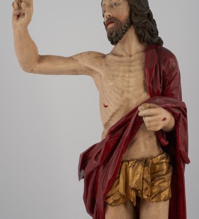 Zdjęcie nr 3: Rzeźba pełna, ustawiona na niskim, kwadratowym, profilowanym cokole. Chrystus ukazany frontalnie, stojący na kawałku zielonej murawy, w kontrapoście, z głową zwróconą w prawo. W lewej, ugiętej ręce trzyma chorągiew; prawa, uniesiona jest wysoko w geście błogosławieństwa. Twarz pociągła, okolona brodą, z na wpół przymkniętymi oczami; włosy długie, kręcone opadają na ramiona. Ciało wychudzone, z zaznaczonymi śladami męki i podkreśloną linią żeber. Przez lewe ramię przerzucony czerwony płaszcz spływający na plecy i z przodu na lewe przedramię; na biodrach złocone  perizonium, ciasno oplecione. Polichromia ciała jest naturalistyczna, perizonium złocone.