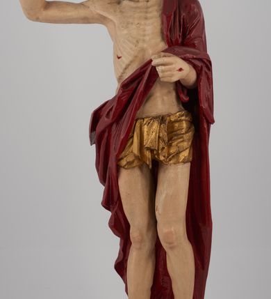 Zdjęcie nr 9: Rzeźba pełna, ustawiona na niskim, kwadratowym, profilowanym cokole. Chrystus ukazany frontalnie, stojący na kawałku zielonej murawy, w kontrapoście, z głową zwróconą w prawo. W lewej, ugiętej ręce trzyma chorągiew; prawa, uniesiona jest wysoko w geście błogosławieństwa. Twarz pociągła, okolona brodą, z na wpół przymkniętymi oczami; włosy długie, kręcone opadają na ramiona. Ciało wychudzone, z zaznaczonymi śladami męki i podkreśloną linią żeber. Przez lewe ramię przerzucony czerwony płaszcz spływający na plecy i z przodu na lewe przedramię; na biodrach złocone  perizonium, ciasno oplecione. Polichromia ciała jest naturalistyczna, perizonium złocone.