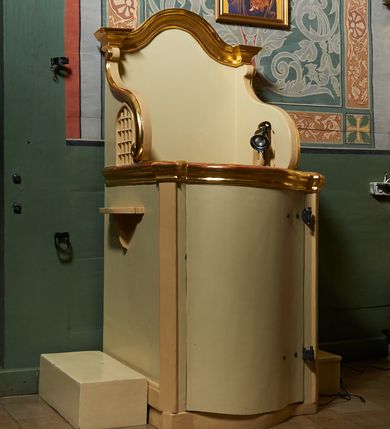 Zdjęcie nr 1: Konfesjonał usytuowany w nawie głównej, przy ścianie północnej. Podstawa na planie zbliżonym do kwadratu, z przodu zakończona linią wklęsło-wypukłą. Drzwi zamykające wejście do siedziska wypukłe, zakończone profilowanym gzymsem, ujęte po bokach ukośnie ustawionymi lizenami. Boczne, występujące ku górze ścianki ograniczające siedzisko zwieńczone fantazyjnymi łukami wklęsło-wypukłymi zakończonymi ślimacznicami. Ściana zaplecka zakończona profilowanym gzymsem w kształcie łuku wklęsło-wypukłego. Po bokach konfesjonału dostawione, wolnostojące klęczniki w formie prostopadłościanów. W ściankach flankujących z boków siedzisko księdza prześwity z grubą kratą, w kształcie stojącego prostokąta, zamkniętego łukiem ostrym, ujęte prostą ramą. Konfesjonał polichromowany w kolorze beżowym, profilowania złocone. 

