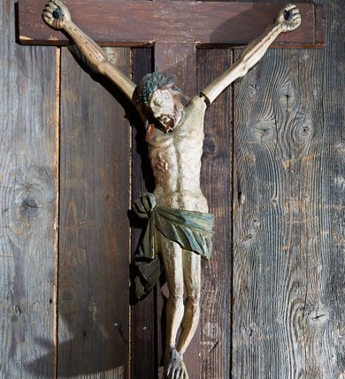 Zdjęcie nr 1: Rzeźba pełna, Chrystus ukazany jako umarły, przybity do krzyża trzema gwoździami. Ciało zawieszone na rozpiętych ramionach o układzie zbliżonym do litery „Y”. Głowa Chrystusa opada na prawe ramię, nogi są delikatnie ugięte w kolanach. Twarz podłużna z zamkniętymi oczami, długim nosem i otwartymi ustami; okolona krótką i brązową brodą. Włosy zawinięte do tyłu i opadające na prawe ramię. Na głowie założona zielona korona cierniowa. Korpus o silnie podkreślonej muskulaturze. W prawym boku głęboka, pionowa rana z zaznaczonymi poniżej wypukłymi kroplami krwi. Perizonium z wywiniętą górną częścią, przewiązane na prawym biodrze i z jednym końcem opadającym wzdłuż prawego uda. Stopy przebite jednym gwoździem, w układzie prawa na lewą. Titulus w formie ukośnie zawieszonej wstęgi o rozdwojonych zakończeniach, w polu napis „INRI”. Polichromia ciała naturalistyczna, perizonium i korona zielone. Krzyż gładki, malowany na brązowo. 
