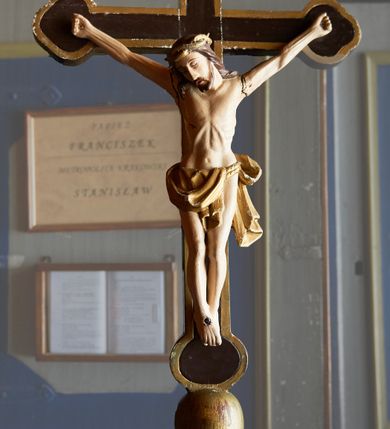 Zdjęcie nr 1: Krzyż procesyjny o długim drzewcu zakończonym gałką, na którym umieszczony jest krucyfiks o trójlistnie zakończonych ramionach. Rzeźba Chrystusa umarłego ułożona w lekkim zwisie, przybita do krzyża trzema gwoździami, ze stopami założonymi prawa na lewą, nogami delikatnie ugiętymi w kolanach i głową przechyloną na prawe ramię. Ciało szczupłe o delikatnie zaznaczonej muskulaturze, podkreślonej linii żeber i wąskiej talii, palce u dłoni silnie zaciśnięte. Twarz podłużna z długim nosem, zamkniętymi oczami, okolona krótkim zarostem; włosy długie, opadające na plecy i prawe ramię; na głowie złocona korona cierniowa spleciona z dwóch gałązek. Perizonium złocone, zawieszone na podwójnym sznurze, odsłaniające lewe biodro, z lewym końcem rozwianym z tyłu lewego uda. Nad głową Chrystusa wisi tabliczka w formie złotej wstęgi z napisem „I.N.R.I.”. Polichromia ciała naturalistyczna, perizonium i korona złocone. Krzyż malowany na brązowo, na brzegach i na gałce na złoto. 

