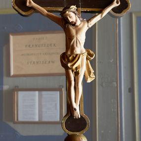 Zdjęcie nr 1: Krzyż procesyjny o długim drzewcu zakończonym gałką, na którym umieszczony jest krucyfiks o trójlistnie zakończonych ramionach. Rzeźba Chrystusa umarłego ułożona w lekkim zwisie, przybita do krzyża trzema gwoździami, ze stopami założonymi prawa na lewą, nogami delikatnie ugiętymi w kolanach i głową przechyloną na prawe ramię. Ciało szczupłe o delikatnie zaznaczonej muskulaturze, podkreślonej linii żeber i wąskiej talii, palce u dłoni silnie zaciśnięte. Twarz podłużna z długim nosem, zamkniętymi oczami, okolona krótkim zarostem; włosy długie, opadające na plecy i prawe ramię; na głowie złocona korona cierniowa spleciona z dwóch gałązek. Perizonium złocone, zawieszone na podwójnym sznurze, odsłaniające lewe biodro, z lewym końcem rozwianym z tyłu lewego uda. Nad głową Chrystusa wisi tabliczka w formie złotej wstęgi z napisem „I.N.R.I.”. Polichromia ciała naturalistyczna, perizonium i korona złocone. Krzyż malowany na brązowo, na brzegach i na gałce na złoto. 

