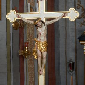 Zdjęcie nr 1: Krzyż procesyjny na długim drzewcu o trójlistnych zakończeniach i złoconym obramowaniu. Figura Chrystusa umarłego ułożona w lekkim zwisie, przybita do krzyża trzema gwoździami, ze stopami założonymi prawa na lewą, nogami delikatnie ugiętymi w kolanach i głową przechyloną na prawe ramię. Twarz szczupła, głęboko rzeźbiona, okolona zarostem, usta otwarte, oczy zamknięte; włosy długie, opadające na ramiona, na głowie korona cierniowa. Ciało szczupłe o delikatnie zaznaczonej muskulaturze i śladami męki. Perizonium złocone, zawiązane na guz na prawym biodrze z silnie drapowanym, zwisającym końcem wzdłuż prawego uda. Nad głową Chrystusa wisi tabliczka w formie białej banderoli w czerwonej, wąskiej ramce z napisem „I.N.R.I.”. Polichromia ciała naturalistyczna, perizonium i korona złocone.

