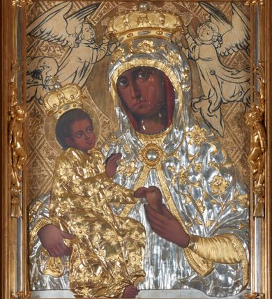 Zdjęcie nr 1: Obraz w kształcie stojącego prostokąta przedstawiający Matkę Boską z Dzieciątkiem. Maria została ukazana w półpostaci z Dzieciątkiem Jezus na prawym ręku, z gruszką w lewej dłoni, z głową delikatnie przechyloną na prawe ramię i wzrokiem skierowanym na widza. Dzieciątko ukazane jest w pozycji siedzącej, zwrócone trzy czwarte w lewo, lewą rączką sięga po gruszkę trzymaną przez Marię w dłoniach, prawą czyni gest błogosławieństwa. Na postacie Marii i Dzieciątka nałożone są metalowe, złocone i srebrzone sukienki, dekorowane w motywy floralne, a także korony w typie zamkniętym. Karnacje bardzo ciemne. Całość ukazana jest na złotym tle, w którym wyróżniają się koliste, złocone nimby wokół głów Marii i Dzieciątka oraz motywy roślinno-geometryczne zamknięte w rombach ukośnej kratownicy. Symetrycznie po bokach głowy Marii zostali przedstawieni konturowaniem dwaj aniołowie koronujący. Obraz umieszczony jest w profilowanej, złoconej i srebrzonej ramie, zdobionej rzeźbiarską, floralną dekoracją oraz parą aniołków na bokach ramy, ukazanych w postawie stojącej, zwróconych ku środkowi obrazu. 