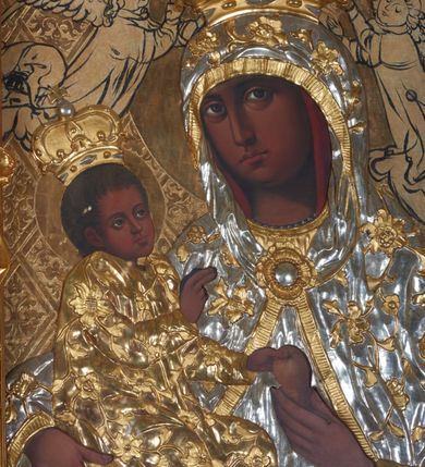 Zdjęcie nr 2: Obraz w kształcie stojącego prostokąta przedstawiający Matkę Boską z Dzieciątkiem. Maria została ukazana w półpostaci z Dzieciątkiem Jezus na prawym ręku, z gruszką w lewej dłoni, z głową delikatnie przechyloną na prawe ramię i wzrokiem skierowanym na widza. Dzieciątko ukazane jest w pozycji siedzącej, zwrócone trzy czwarte w lewo, lewą rączką sięga po gruszkę trzymaną przez Marię w dłoniach, prawą czyni gest błogosławieństwa. Na postacie Marii i Dzieciątka nałożone są metalowe, złocone i srebrzone sukienki, dekorowane w motywy floralne, a także korony w typie zamkniętym. Karnacje bardzo ciemne. Całość ukazana jest na złotym tle, w którym wyróżniają się koliste, złocone nimby wokół głów Marii i Dzieciątka oraz motywy roślinno-geometryczne zamknięte w rombach ukośnej kratownicy. Symetrycznie po bokach głowy Marii zostali przedstawieni konturowaniem dwaj aniołowie koronujący. Obraz umieszczony jest w profilowanej, złoconej i srebrzonej ramie, zdobionej rzeźbiarską, floralną dekoracją oraz parą aniołków na bokach ramy, ukazanych w postawie stojącej, zwróconych ku środkowi obrazu. 