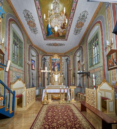 Zdjęcie nr 3: Ława ustawiona na niskim prostopadłościennym podeście, jednorzędowa, trójosobowa, z zapleckiem i z przedpiersiem, zwieńczona dwiema wolutami spinającymi pośrodku palmetę oraz małymi wazonikami ustawionymi na skrajach zaplecka. Przedpiersie przedzielone na trzy płyciny w kształcie stojących prostokątów zdobione w polu stylizowaną wicią z motywami ornamentu pseudoregencyjnego. Zaplecek przedzielony na dwie strefy; w dolnej zdobiony trzema kwadratowymi płycinami, w górnej płyciną w kształcie leżącego prostokąta zamkniętego od góry łukiem wklęsło-wypukłym. 
