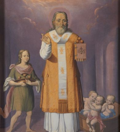 Zdjęcie nr 1: Obraz w kształcie stojącego prostokąta przedstawiający św. Mikołaja. Święty został ukazany frontalnie, całopostaciowo w centrum kompozycji. W lewej ręce trzyma księgę, na której ustawione są trzy złote kule; prawą ręką czyni gest błogosławieństwa. Święty Mikołaj ma szeroką twarz, okoloną siwą, średniej długości brodą, nos długi i wąski, oczy małe, skierowane w dal. Włosy długie, siwe, z przedziałkiem pośrodku, opadające lokami na plecy. Ubrany jest w szaty biskupie: białą albę, złoty ornat, palice na bokach i omoforion, wokół głowy ma kolisty nimb. Po lewej stronie znajduje się chłopiec w postawie stojącej, który trzyma w dłoniach złotą misę, a na niej kielich i dwa małe puchary. Ma owalną twarz z wyraźnie zaznaczonym podbródkiem, długi i szeroki nos, małe oczy oraz długie, falowane włosy opadające na plecy. Ubrany jest w zieloną tunikę do kolan z podwiniętymi szerokimi rękawami oraz czerwony, zwiewny płaszcz spięty małą broszą na prawym ramieniu. Po prawej stronie ukazano szaflik z trójką półnagich małych dzieci. Księga trzymana w rękach przez św. Mikołaja ma czerwoną obwolutę i jest spięta dwiema klamrami, na okładce znajduje się monogram IHS zwieńczony krzyżykiem, a poniżej gorejące serce. Całość została ukazana we wnętrzu architektonicznym, górną część obrazu pokrywa pochmurne niebo. Kolorystyka jasna i stonowana.
