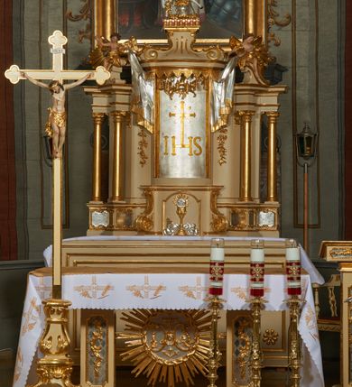 Zdjęcie nr 1: Ołtarz murowany, w formie prostopadłościanu. Mensa drewniana z portatylem. Antependium złocone, w formie leżącego prostokąta w profilowanej ramie; w polu środkowym znajduje się monogram IHS, a w narożach rozety. Tabernakulum z wypukłą ścianką frontową, po bokach ujęte jest spływami wolutowymi na cokołach, dekorowanymi ornamentem rocaille&#039;owym. Drzwiczki w formie stojącego prostokąta zamkniętego łukiem nadwieszonym; w polu mają płaskorzeźbiony kielich wśród obłoków, z hostią w glorii. Tron wystawienia architektoniczny, trójosiowy, jednokondygnacyjny ze zwieńczeniem. Oś środkowa wypukła, wyższa niż boczne, zamknięta jest profilowanym gzymsem. Tron ujmują dwie pary kolumn na ukośnie ustawionych cokołach. Podpory dźwigają pełne belkowanie wyłamane na ich osi. Na linii wewnętrznych kolumn znajduje się przerywany przyczółek z siedzącymi aniołkami podtrzymującymi srebrzony paludament. Zwieńczenie ma formę cokołu, ujętego spływami wolutowymi; na którym ustawiona jest księga zamknięta na siedem pięczęci, na niej postawiona srebrzona waza z kwiatami oraz biały baranek z chorągwią paschalną. Na cokołach wspierających kolumny znajdują się rocaille&#039;owe płyciny z lusterkami. Oś środkowa flankowana jest kwiatowymi zwisami. Tron wystawienia posiada obrotową wnękę z gzymsem wieńczącym, ozdobionym lambrekinem: awers wklęsły, posrebrzany, z rytym monogramem IHS oraz krzyżem i wiązkami promieni, powyżej rzeźbiony rocaille; rewers w kształcie niszy, dekorowany rytą, złoconą kratką i rzeźbionym, srebrzonym rocaille&#039;m. Struktura polichromowana na beżowo, kolumny, ornamentyka i profilowania złocone, detale srebrzone. Za ołtarzem, na wschodniej ścianie prezbiterium wisi obraz św. Erazma w złoconej, profilowanej ramie, w formie stojącego prostokąta, zamkniętego nadwieszonym łukiem półkolistym. Rama dekorowana jest w narożach i na bokach stylizowanymi palmetami. Nad obrazem, w podłuczu znajduje się płaskorzeźbiona korona otwarta z dwoma piórami.