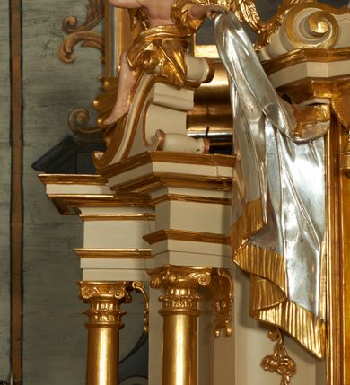 Zdjęcie nr 6: Ołtarz murowany, w formie prostopadłościanu. Mensa drewniana z portatylem. Antependium złocone, w formie leżącego prostokąta w profilowanej ramie; w polu środkowym znajduje się monogram IHS, a w narożach rozety. Tabernakulum z wypukłą ścianką frontową, po bokach ujęte jest spływami wolutowymi na cokołach, dekorowanymi ornamentem rocaille'owym. Drzwiczki w formie stojącego prostokąta zamkniętego łukiem nadwieszonym; w polu mają płaskorzeźbiony kielich wśród obłoków, z hostią w glorii. Tron wystawienia architektoniczny, trójosiowy, jednokondygnacyjny ze zwieńczeniem. Oś środkowa wypukła, wyższa niż boczne, zamknięta jest profilowanym gzymsem. Tron ujmują dwie pary kolumn na ukośnie ustawionych cokołach. Podpory dźwigają pełne belkowanie wyłamane na ich osi. Na linii wewnętrznych kolumn znajduje się przerywany przyczółek z siedzącymi aniołkami podtrzymującymi srebrzony paludament. Zwieńczenie ma formę cokołu, ujętego spływami wolutowymi; na którym ustawiona jest księga zamknięta na siedem pięczęci, na niej postawiona srebrzona waza z kwiatami oraz biały baranek z chorągwią paschalną. Na cokołach wspierających kolumny znajdują się rocaille'owe płyciny z lusterkami. Oś środkowa flankowana jest kwiatowymi zwisami. Tron wystawienia posiada obrotową wnękę z gzymsem wieńczącym, ozdobionym lambrekinem: awers wklęsły, posrebrzany, z rytym monogramem IHS oraz krzyżem i wiązkami promieni, powyżej rzeźbiony rocaille; rewers w kształcie niszy, dekorowany rytą, złoconą kratką i rzeźbionym, srebrzonym rocaille'm. Struktura polichromowana na beżowo, kolumny, ornamentyka i profilowania złocone, detale srebrzone. Za ołtarzem, na wschodniej ścianie prezbiterium wisi obraz św. Erazma w złoconej, profilowanej ramie, w formie stojącego prostokąta, zamkniętego nadwieszonym łukiem półkolistym. Rama dekorowana jest w narożach i na bokach stylizowanymi palmetami. Nad obrazem, w podłuczu znajduje się płaskorzeźbiona korona otwarta z dwoma piórami.