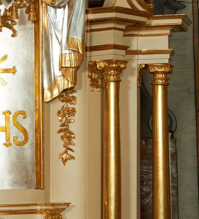 Zdjęcie nr 7: Ołtarz murowany, w formie prostopadłościanu. Mensa drewniana z portatylem. Antependium złocone, w formie leżącego prostokąta w profilowanej ramie; w polu środkowym znajduje się monogram IHS, a w narożach rozety. Tabernakulum z wypukłą ścianką frontową, po bokach ujęte jest spływami wolutowymi na cokołach, dekorowanymi ornamentem rocaille'owym. Drzwiczki w formie stojącego prostokąta zamkniętego łukiem nadwieszonym; w polu mają płaskorzeźbiony kielich wśród obłoków, z hostią w glorii. Tron wystawienia architektoniczny, trójosiowy, jednokondygnacyjny ze zwieńczeniem. Oś środkowa wypukła, wyższa niż boczne, zamknięta jest profilowanym gzymsem. Tron ujmują dwie pary kolumn na ukośnie ustawionych cokołach. Podpory dźwigają pełne belkowanie wyłamane na ich osi. Na linii wewnętrznych kolumn znajduje się przerywany przyczółek z siedzącymi aniołkami podtrzymującymi srebrzony paludament. Zwieńczenie ma formę cokołu, ujętego spływami wolutowymi; na którym ustawiona jest księga zamknięta na siedem pięczęci, na niej postawiona srebrzona waza z kwiatami oraz biały baranek z chorągwią paschalną. Na cokołach wspierających kolumny znajdują się rocaille'owe płyciny z lusterkami. Oś środkowa flankowana jest kwiatowymi zwisami. Tron wystawienia posiada obrotową wnękę z gzymsem wieńczącym, ozdobionym lambrekinem: awers wklęsły, posrebrzany, z rytym monogramem IHS oraz krzyżem i wiązkami promieni, powyżej rzeźbiony rocaille; rewers w kształcie niszy, dekorowany rytą, złoconą kratką i rzeźbionym, srebrzonym rocaille'm. Struktura polichromowana na beżowo, kolumny, ornamentyka i profilowania złocone, detale srebrzone. Za ołtarzem, na wschodniej ścianie prezbiterium wisi obraz św. Erazma w złoconej, profilowanej ramie, w formie stojącego prostokąta, zamkniętego nadwieszonym łukiem półkolistym. Rama dekorowana jest w narożach i na bokach stylizowanymi palmetami. Nad obrazem, w podłuczu znajduje się płaskorzeźbiona korona otwarta z dwoma piórami.