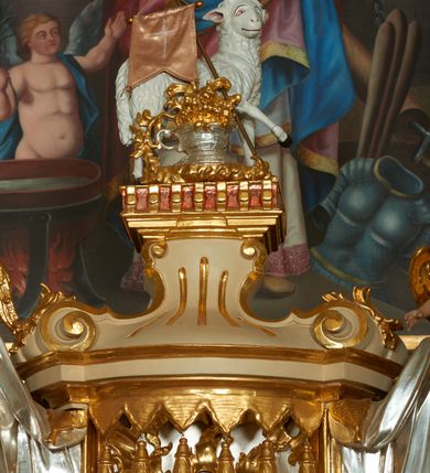 Zdjęcie nr 8: Ołtarz murowany, w formie prostopadłościanu. Mensa drewniana z portatylem. Antependium złocone, w formie leżącego prostokąta w profilowanej ramie; w polu środkowym znajduje się monogram IHS, a w narożach rozety. Tabernakulum z wypukłą ścianką frontową, po bokach ujęte jest spływami wolutowymi na cokołach, dekorowanymi ornamentem rocaille'owym. Drzwiczki w formie stojącego prostokąta zamkniętego łukiem nadwieszonym; w polu mają płaskorzeźbiony kielich wśród obłoków, z hostią w glorii. Tron wystawienia architektoniczny, trójosiowy, jednokondygnacyjny ze zwieńczeniem. Oś środkowa wypukła, wyższa niż boczne, zamknięta jest profilowanym gzymsem. Tron ujmują dwie pary kolumn na ukośnie ustawionych cokołach. Podpory dźwigają pełne belkowanie wyłamane na ich osi. Na linii wewnętrznych kolumn znajduje się przerywany przyczółek z siedzącymi aniołkami podtrzymującymi srebrzony paludament. Zwieńczenie ma formę cokołu, ujętego spływami wolutowymi; na którym ustawiona jest księga zamknięta na siedem pięczęci, na niej postawiona srebrzona waza z kwiatami oraz biały baranek z chorągwią paschalną. Na cokołach wspierających kolumny znajdują się rocaille'owe płyciny z lusterkami. Oś środkowa flankowana jest kwiatowymi zwisami. Tron wystawienia posiada obrotową wnękę z gzymsem wieńczącym, ozdobionym lambrekinem: awers wklęsły, posrebrzany, z rytym monogramem IHS oraz krzyżem i wiązkami promieni, powyżej rzeźbiony rocaille; rewers w kształcie niszy, dekorowany rytą, złoconą kratką i rzeźbionym, srebrzonym rocaille'm. Struktura polichromowana na beżowo, kolumny, ornamentyka i profilowania złocone, detale srebrzone. Za ołtarzem, na wschodniej ścianie prezbiterium wisi obraz św. Erazma w złoconej, profilowanej ramie, w formie stojącego prostokąta, zamkniętego nadwieszonym łukiem półkolistym. Rama dekorowana jest w narożach i na bokach stylizowanymi palmetami. Nad obrazem, w podłuczu znajduje się płaskorzeźbiona korona otwarta z dwoma piórami.