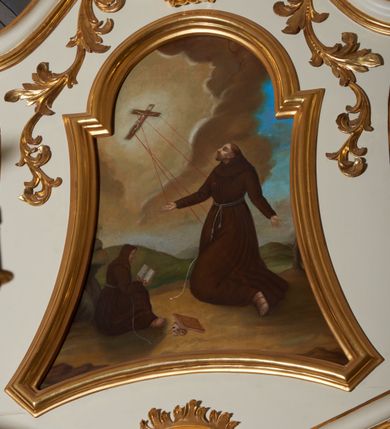 Zdjęcie nr 2: Obraz w kształcie stojącego prostokąta o wklęsłych bokach, od góry zamkniętego łukiem półkolistym, nadwieszonym. W centrum kompozycji przedstawienie klęczącego św. Franciszka otrzymującego stygmaty; głowa uniesiona lekko ku górze, ręce rozłożone szeroko na boki. Twarz widoczna z lewego profilu, okolona krótką i spiczasto zakończoną brodą, długi i prosty nos, małe oczy, na głowie tonsura. Święty ubrany jest w habit franciszkański, przewiązany sznurem. Przed nim, przy skałach siedzi czytający zakonnik w brązowym habicie, obok leżą zamknięta księga i czaszka. W oddali widoczny pejzaż górski. W lewym, górnym narożu postać ukrzyżowanego Chrystusa, z którego ran wychodzą czerwone promienie, tworzące stygmaty u św. Franciszka. W tle brunatno-żółte chmury na błękitnym niebie. Kolorystyka jasna, ciepła. Rama obrazu profilowana i złocona.