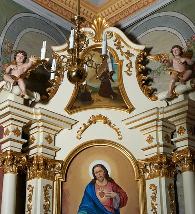 Zdjęcie nr 3: Obraz w kształcie stojącego prostokąta o wklęsłych bokach, od góry zamkniętego łukiem półkolistym, nadwieszonym. W centrum kompozycji przedstawienie klęczącego św. Franciszka otrzymującego stygmaty; głowa uniesiona lekko ku górze, ręce rozłożone szeroko na boki. Twarz widoczna z lewego profilu, okolona krótką i spiczasto zakończoną brodą, długi i prosty nos, małe oczy, na głowie tonsura. Święty ubrany jest w habit franciszkański, przewiązany sznurem. Przed nim, przy skałach siedzi czytający zakonnik w brązowym habicie, obok leżą zamknięta księga i czaszka. W oddali widoczny pejzaż górski. W lewym, górnym narożu postać ukrzyżowanego Chrystusa, z którego ran wychodzą czerwone promienie, tworzące stygmaty u św. Franciszka. W tle brunatno-żółte chmury na błękitnym niebie. Kolorystyka jasna, ciepła. Rama obrazu profilowana i złocona.