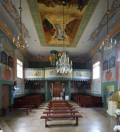 Zdjęcie nr 2: Organy architektoniczne, jednokondygnacyjne, pięcioosiowe. Oś środkowa i skrajne są wypukłe, wydzielone wielobocznymi ryzalitami z prześwitami wypełnionymi piszczałkami; zwieńczone profilowanym gzymsem z uskokami. Analogicznie ukształtowany gzyms ujmuje strukturę od dołu. Ryzality zewnętrzne sięgają stropu, środkowy niższy połączony jest z nimi płaskimi ściankami z prześwitami na piszczałki. Na ścianach bocznych organów płyciny mają ażurową kratkę. Organy ujęte są ażurowymi uszami utworzonymi z rocaille&#039;ów. Oś środkowa ze zwieńczeniem w postaci muszli. Przestrzeń między ryzalitami oraz prześwity w górnej partii wypełniają stylizowane liście akantu. Struktura polichromowana w kolorze ciemnego turkusu; ornamentyka złocona.