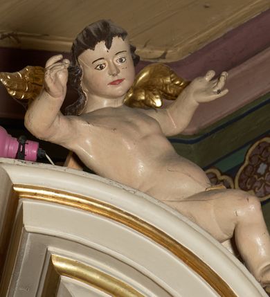 Zdjęcie nr 24: Ołtarz typu architektonicznego, jednokondygnacyjny, jednoosiowy, z bramkami i ze zwieńczeniem w formie glorii. Mensa prostopadłościenna, na ściance przedniej zdobiona rzędem płycin w kształcie stojącego prostokąta, zamkniętych łukiem nadwieszonym. W polu środkowej płyciny malowany krzyż grecki, w pozostałych gałązki białych lilii. Tabernakulum w formie prostopadłościennej skrzynki, z częścią środkową wysuniętą do przodu, zamknięte od góry profilowanym gzymsem w kształcie łuku nadwieszonego. Drzwiczki metalowe, pośrodku dekorowane płyciną w kształcie stojącego prostokąta, zamkniętego łukiem nadwieszonym, w polu kielich z hostią, kłosy zboża i kiście winogron. Nad tabernakulum tron wystawienia na tle promienistej glorii z monogramem IHS pośrodku, po bokach flankowany przez parę aniołków usadzonych na wolutach. Retabulum ustawione na wysokim cokole, ujęte parą zdwojonych, ukośnie ustawionych pilastrów podtrzymujących przerywane belkowanie, na którym usadzona para putt. Trzony pilastrów zdobione kanelowaniem, kapitele stylizowane, kompozytowe. Putto po lewej stronie z otwartą księgą, w której znajduje się napis: „Assu/pta / est / Maria / in / Caelum”. W polu głównym nastawy, na wysokości dwóch trzecich obraz z przedstawieniem Wniebowzięcia Najświętszej Marii Panny. Po bokach obrazu para rzeźbionych aniołków. W zwieńczeniu płaskorzeźba Boga Ojca na tle promienistej glorii. Drzwiczki bramek zdobione płyciną w kształcie stojącego prostokąta, zamkniętą od góry łukiem nadwieszonym. Zwieńczenie bramek zdobione festonem z liści wawrzynu, zakończone niskim cokołem, na którym ustawione rzeźby: po lewej św. Jana Chrzciciela, po prawej św. Kazimierza. Uszy ażurowe w postaci ornamentu rocaille'owego. Struktura ołtarza w kolorze beżowym, ornamentyka, detale i profilowania złocone.