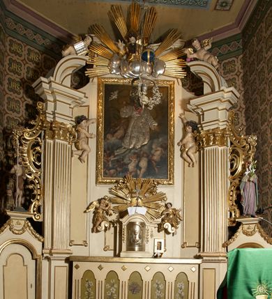 Zdjęcie nr 2: Ołtarz typu architektonicznego, jednokondygnacyjny, jednoosiowy, z bramkami i ze zwieńczeniem w formie glorii. Mensa prostopadłościenna, na ściance przedniej zdobiona rzędem płycin w kształcie stojącego prostokąta, zamkniętych łukiem nadwieszonym. W polu środkowej płyciny malowany krzyż grecki, w pozostałych gałązki białych lilii. Tabernakulum w formie prostopadłościennej skrzynki, z częścią środkową wysuniętą do przodu, zamknięte od góry profilowanym gzymsem w kształcie łuku nadwieszonego. Drzwiczki metalowe, pośrodku dekorowane płyciną w kształcie stojącego prostokąta, zamkniętego łukiem nadwieszonym, w polu kielich z hostią, kłosy zboża i kiście winogron. Nad tabernakulum tron wystawienia na tle promienistej glorii z monogramem IHS pośrodku, po bokach flankowany przez parę aniołków usadzonych na wolutach. Retabulum ustawione na wysokim cokole, ujęte parą zdwojonych, ukośnie ustawionych pilastrów podtrzymujących przerywane belkowanie, na którym usadzona para putt. Trzony pilastrów zdobione kanelowaniem, kapitele stylizowane, kompozytowe. Putto po lewej stronie z otwartą księgą, w której znajduje się napis: „Assu/pta / est / Maria / in / Caelum”. W polu głównym nastawy, na wysokości dwóch trzecich obraz z przedstawieniem Wniebowzięcia Najświętszej Marii Panny. Po bokach obrazu para rzeźbionych aniołków. W zwieńczeniu płaskorzeźba Boga Ojca na tle promienistej glorii. Drzwiczki bramek zdobione płyciną w kształcie stojącego prostokąta, zamkniętą od góry łukiem nadwieszonym. Zwieńczenie bramek zdobione festonem z liści wawrzynu, zakończone niskim cokołem, na którym ustawione rzeźby: po lewej św. Jana Chrzciciela, po prawej św. Kazimierza. Uszy ażurowe w postaci ornamentu rocaille'owego. Struktura ołtarza w kolorze beżowym, ornamentyka, detale i profilowania złocone.