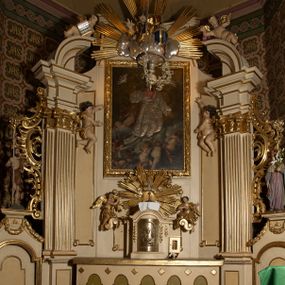 Zdjęcie nr 1: Ołtarz typu architektonicznego, jednokondygnacyjny, jednoosiowy, z bramkami i ze zwieńczeniem w formie glorii. Mensa prostopadłościenna, na ściance przedniej zdobiona rzędem płycin w kształcie stojącego prostokąta, zamkniętych łukiem nadwieszonym. W polu środkowej płyciny malowany krzyż grecki, w pozostałych gałązki białych lilii. Tabernakulum w formie prostopadłościennej skrzynki, z częścią środkową wysuniętą do przodu, zamknięte od góry profilowanym gzymsem w kształcie łuku nadwieszonego. Drzwiczki metalowe, pośrodku dekorowane płyciną w kształcie stojącego prostokąta, zamkniętego łukiem nadwieszonym, w polu kielich z hostią, kłosy zboża i kiście winogron. Nad tabernakulum tron wystawienia na tle promienistej glorii z monogramem IHS pośrodku, po bokach flankowany przez parę aniołków usadzonych na wolutach. Retabulum ustawione na wysokim cokole, ujęte parą zdwojonych, ukośnie ustawionych pilastrów podtrzymujących przerywane belkowanie, na którym usadzona para putt. Trzony pilastrów zdobione kanelowaniem, kapitele stylizowane, kompozytowe. Putto po lewej stronie z otwartą księgą, w której znajduje się napis: „Assu/pta / est / Maria / in / Caelum”. W polu głównym nastawy, na wysokości dwóch trzecich obraz z przedstawieniem Wniebowzięcia Najświętszej Marii Panny. Po bokach obrazu para rzeźbionych aniołków. W zwieńczeniu płaskorzeźba Boga Ojca na tle promienistej glorii. Drzwiczki bramek zdobione płyciną w kształcie stojącego prostokąta, zamkniętą od góry łukiem nadwieszonym. Zwieńczenie bramek zdobione festonem z liści wawrzynu, zakończone niskim cokołem, na którym ustawione rzeźby: po lewej św. Jana Chrzciciela, po prawej św. Kazimierza. Uszy ażurowe w postaci ornamentu rocaille'owego. Struktura ołtarza w kolorze beżowym, ornamentyka, detale i profilowania złocone.