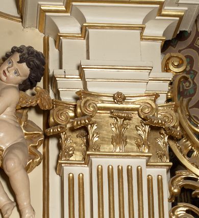 Zdjęcie nr 4: Ołtarz typu architektonicznego, jednokondygnacyjny, jednoosiowy, z bramkami i ze zwieńczeniem w formie glorii. Mensa prostopadłościenna, na ściance przedniej zdobiona rzędem płycin w kształcie stojącego prostokąta, zamkniętych łukiem nadwieszonym. W polu środkowej płyciny malowany krzyż grecki, w pozostałych gałązki białych lilii. Tabernakulum w formie prostopadłościennej skrzynki, z częścią środkową wysuniętą do przodu, zamknięte od góry profilowanym gzymsem w kształcie łuku nadwieszonego. Drzwiczki metalowe, pośrodku dekorowane płyciną w kształcie stojącego prostokąta, zamkniętego łukiem nadwieszonym, w polu kielich z hostią, kłosy zboża i kiście winogron. Nad tabernakulum tron wystawienia na tle promienistej glorii z monogramem IHS pośrodku, po bokach flankowany przez parę aniołków usadzonych na wolutach. Retabulum ustawione na wysokim cokole, ujęte parą zdwojonych, ukośnie ustawionych pilastrów podtrzymujących przerywane belkowanie, na którym usadzona para putt. Trzony pilastrów zdobione kanelowaniem, kapitele stylizowane, kompozytowe. Putto po lewej stronie z otwartą księgą, w której znajduje się napis: „Assu/pta / est / Maria / in / Caelum”. W polu głównym nastawy, na wysokości dwóch trzecich obraz z przedstawieniem Wniebowzięcia Najświętszej Marii Panny. Po bokach obrazu para rzeźbionych aniołków. W zwieńczeniu płaskorzeźba Boga Ojca na tle promienistej glorii. Drzwiczki bramek zdobione płyciną w kształcie stojącego prostokąta, zamkniętą od góry łukiem nadwieszonym. Zwieńczenie bramek zdobione festonem z liści wawrzynu, zakończone niskim cokołem, na którym ustawione rzeźby: po lewej św. Jana Chrzciciela, po prawej św. Kazimierza. Uszy ażurowe w postaci ornamentu rocaille&#039;owego. Struktura ołtarza w kolorze beżowym, ornamentyka, detale i profilowania złocone.