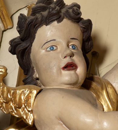 Zdjęcie nr 9: Ołtarz typu architektonicznego, jednokondygnacyjny, jednoosiowy, z bramkami i ze zwieńczeniem w formie glorii. Mensa prostopadłościenna, na ściance przedniej zdobiona rzędem płycin w kształcie stojącego prostokąta, zamkniętych łukiem nadwieszonym. W polu środkowej płyciny malowany krzyż grecki, w pozostałych gałązki białych lilii. Tabernakulum w formie prostopadłościennej skrzynki, z częścią środkową wysuniętą do przodu, zamknięte od góry profilowanym gzymsem w kształcie łuku nadwieszonego. Drzwiczki metalowe, pośrodku dekorowane płyciną w kształcie stojącego prostokąta, zamkniętego łukiem nadwieszonym, w polu kielich z hostią, kłosy zboża i kiście winogron. Nad tabernakulum tron wystawienia na tle promienistej glorii z monogramem IHS pośrodku, po bokach flankowany przez parę aniołków usadzonych na wolutach. Retabulum ustawione na wysokim cokole, ujęte parą zdwojonych, ukośnie ustawionych pilastrów podtrzymujących przerywane belkowanie, na którym usadzona para putt. Trzony pilastrów zdobione kanelowaniem, kapitele stylizowane, kompozytowe. Putto po lewej stronie z otwartą księgą, w której znajduje się napis: „Assu/pta / est / Maria / in / Caelum”. W polu głównym nastawy, na wysokości dwóch trzecich obraz z przedstawieniem Wniebowzięcia Najświętszej Marii Panny. Po bokach obrazu para rzeźbionych aniołków. W zwieńczeniu płaskorzeźba Boga Ojca na tle promienistej glorii. Drzwiczki bramek zdobione płyciną w kształcie stojącego prostokąta, zamkniętą od góry łukiem nadwieszonym. Zwieńczenie bramek zdobione festonem z liści wawrzynu, zakończone niskim cokołem, na którym ustawione rzeźby: po lewej św. Jana Chrzciciela, po prawej św. Kazimierza. Uszy ażurowe w postaci ornamentu rocaille&#039;owego. Struktura ołtarza w kolorze beżowym, ornamentyka, detale i profilowania złocone.