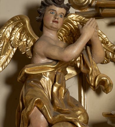 Zdjęcie nr 15: Ołtarz typu architektonicznego, jednokondygnacyjny, jednoosiowy, z bramkami i ze zwieńczeniem w formie glorii. Mensa prostopadłościenna, na ściance przedniej zdobiona rzędem płycin w kształcie stojącego prostokąta, zamkniętych łukiem nadwieszonym. W polu środkowej płyciny malowany krzyż grecki, w pozostałych gałązki białych lilii. Tabernakulum w formie prostopadłościennej skrzynki, z częścią środkową wysuniętą do przodu, zamknięte od góry profilowanym gzymsem w kształcie łuku nadwieszonego. Drzwiczki metalowe, pośrodku dekorowane płyciną w kształcie stojącego prostokąta, zamkniętego łukiem nadwieszonym, w polu kielich z hostią, kłosy zboża i kiście winogron. Nad tabernakulum tron wystawienia na tle promienistej glorii z monogramem IHS pośrodku, po bokach flankowany przez parę aniołków usadzonych na wolutach. Retabulum ustawione na wysokim cokole, ujęte parą zdwojonych, ukośnie ustawionych pilastrów podtrzymujących przerywane belkowanie, na którym usadzona para putt. Trzony pilastrów zdobione kanelowaniem, kapitele stylizowane, kompozytowe. Putto po lewej stronie z otwartą księgą, w której znajduje się napis: „Assu/pta / est / Maria / in / Caelum”. W polu głównym nastawy, na wysokości dwóch trzecich obraz z przedstawieniem Wniebowzięcia Najświętszej Marii Panny. Po bokach obrazu para rzeźbionych aniołków. W zwieńczeniu płaskorzeźba Boga Ojca na tle promienistej glorii. Drzwiczki bramek zdobione płyciną w kształcie stojącego prostokąta, zamkniętą od góry łukiem nadwieszonym. Zwieńczenie bramek zdobione festonem z liści wawrzynu, zakończone niskim cokołem, na którym ustawione rzeźby: po lewej św. Jana Chrzciciela, po prawej św. Kazimierza. Uszy ażurowe w postaci ornamentu rocaille'owego. Struktura ołtarza w kolorze beżowym, ornamentyka, detale i profilowania złocone.