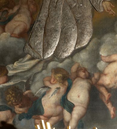 Zdjęcie nr 8: Obraz w kształcie stojącego prostokąta z przedstawieniem Wniebowzięcia Najświętszej Marii Panny. W centrum kompozycji ukazana Matka Boska unosząca się na chmurze obłoków, z ugiętymi w kolanach nogami, z prawą ręką wzniesioną do góry, lewą odsuniętą w bok, z głową lekko uniesioną do góry. Strój zasłonięty metalową, trybowaną sukienką. Twarz szeroka, z długim i wąskim nosem, wzrokiem skierowanym ku górze, włosy ciemne schowane pod metalową koroną; u szyi trzy sznury czerwonych korali. Wokół głowy nimb ze złotych gwiazd, a na głowie metalowa korona zamknięta. W dolnej części kompozycji grupka nagich putt w ekspresyjnych pozach, ukazane z różnych ujęć, z akcentem zielonej tkaniny, która przebiega pomiędzy nimi. Druga grupka putt nieco wyżej, po lewej stronie obrazu: jedno trzyma wianek, drugie zieloną gałązkę palmy. W górnej części obrazu, po bokach Marii, przybite dwa aniołki z blachy. Sukienka ozdobiona grawerowaną, bujną wicią roślinną z wielopłatkowymi kwiatami i liśćmi akantu. Tło ciemne w odcieniach szarości i brązu.

