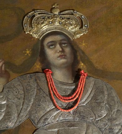 Zdjęcie nr 6: Obraz w kształcie stojącego prostokąta z przedstawieniem Wniebowzięcia Najświętszej Marii Panny. W centrum kompozycji ukazana Matka Boska unosząca się na chmurze obłoków, z ugiętymi w kolanach nogami, z prawą ręką wzniesioną do góry, lewą odsuniętą w bok, z głową lekko uniesioną do góry. Strój zasłonięty metalową, trybowaną sukienką. Twarz szeroka, z długim i wąskim nosem, wzrokiem skierowanym ku górze, włosy ciemne schowane pod metalową koroną; u szyi trzy sznury czerwonych korali. Wokół głowy nimb ze złotych gwiazd, a na głowie metalowa korona zamknięta. W dolnej części kompozycji grupka nagich putt w ekspresyjnych pozach, ukazane z różnych ujęć, z akcentem zielonej tkaniny, która przebiega pomiędzy nimi. Druga grupka putt nieco wyżej, po lewej stronie obrazu: jedno trzyma wianek, drugie zieloną gałązkę palmy. W górnej części obrazu, po bokach Marii, przybite dwa aniołki z blachy. Sukienka ozdobiona grawerowaną, bujną wicią roślinną z wielopłatkowymi kwiatami i liśćmi akantu. Tło ciemne w odcieniach szarości i brązu.

