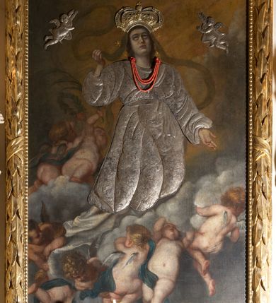 Zdjęcie nr 2: Obraz w kształcie stojącego prostokąta z przedstawieniem Wniebowzięcia Najświętszej Marii Panny. W centrum kompozycji ukazana Matka Boska unosząca się na chmurze obłoków, z ugiętymi w kolanach nogami, z prawą ręką wzniesioną do góry, lewą odsuniętą w bok, z głową lekko uniesioną do góry. Strój zasłonięty metalową, trybowaną sukienką. Twarz szeroka, z długim i wąskim nosem, wzrokiem skierowanym ku górze, włosy ciemne schowane pod metalową koroną; u szyi trzy sznury czerwonych korali. Wokół głowy nimb ze złotych gwiazd, a na głowie metalowa korona zamknięta. W dolnej części kompozycji grupka nagich putt w ekspresyjnych pozach, ukazane z różnych ujęć, z akcentem zielonej tkaniny, która przebiega pomiędzy nimi. Druga grupka putt nieco wyżej, po lewej stronie obrazu: jedno trzyma wianek, drugie zieloną gałązkę palmy. W górnej części obrazu, po bokach Marii, przybite dwa aniołki z blachy. Sukienka ozdobiona grawerowaną, bujną wicią roślinną z wielopłatkowymi kwiatami i liśćmi akantu. Tło ciemne w odcieniach szarości i brązu.

