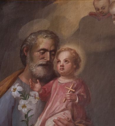Zdjęcie nr 3: Obraz w kształcie stojącego prostokąta przedstawiający św. Józefa z Dzieciątkiem. Święty został ukazany w całej postaci, delikatnie zwrócony w lewo. Na lewej ręce trzyma Dzieciątko Jezus, a w prawej gałązkę białej lilii. Święty Józef ma szeroką twarz, okoloną krótką i siwą brodą oraz siwe włosy, nos długi i wąski, wzrok wpatrzony w Jezusa. Ubrany jest w niebieską szatę z długimi rękawami oraz ugrowy płaszcz; na stopach ma sandały. Dzieciątko ma twarz o rysach niemowlęcych, wzrok skierowany ku górze. Zwrócone jest w trzech czwartych w prawo, ukazane w pozycji siedzącej, z krzyżykiem łacińskim w lewej dłoni, z prawą rączką wyciągniętą przed siebie. Ubrane w jasnoróżową sukienkę z długimi rękawami. Wokół głów św. Józefa i Dzieciątka znajdują się złote nimby. Całość ukazana w sumarycznie oddanym wnętrzu architektonicznym z arkadą otwartą na pejzaż górski. W prawym górnym narożu dwie uskrzydlone główki anielskie na chmurze obłoków. 
