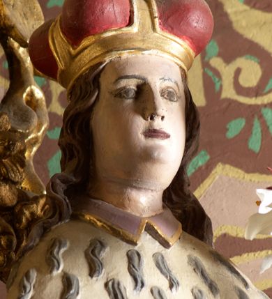 Zdjęcie nr 3: Rzeźba wolnostojąca, ukazująca św. Kazimierza, ustawiona na niskim cokole. Święty przedstawiony w całej postaci, w postawie stojącej z gałązką białej lilii w lewej dłoni, prawą dłonią przytrzymujący połę płaszcza. Twarz owalna, z wyraźnie zaznaczonym podbródkiem, z wąskimi ustami i wzrokiem skierowanym przed siebie; włosy długie i ciemnobrązowe opadające na plecy. Ubrany jest w długą, fioletową suknię z długimi rękawami, czerwony płaszcz z zieloną podszewką i gronostajową pelerynką, mitrę książęcą, zwieńczoną krzyżykiem na głowie oraz krzyżyk zawieszony na piersi na długim łańcuszku, na stopach buty. Polichromia w odsłoniętych partiach ciała naturalistyczna. 

