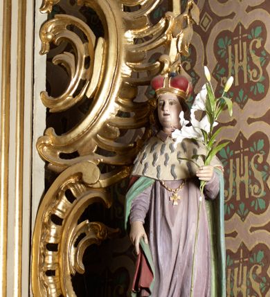 Zdjęcie nr 2: Rzeźba wolnostojąca, ukazująca św. Kazimierza, ustawiona na niskim cokole. Święty przedstawiony w całej postaci, w postawie stojącej z gałązką białej lilii w lewej dłoni, prawą dłonią przytrzymujący połę płaszcza. Twarz owalna, z wyraźnie zaznaczonym podbródkiem, z wąskimi ustami i wzrokiem skierowanym przed siebie; włosy długie i ciemnobrązowe opadające na plecy. Ubrany jest w długą, fioletową suknię z długimi rękawami, czerwony płaszcz z zieloną podszewką i gronostajową pelerynką, mitrę książęcą, zwieńczoną krzyżykiem na głowie oraz krzyżyk zawieszony na piersi na długim łańcuszku, na stopach buty. Polichromia w odsłoniętych partiach ciała naturalistyczna. 

