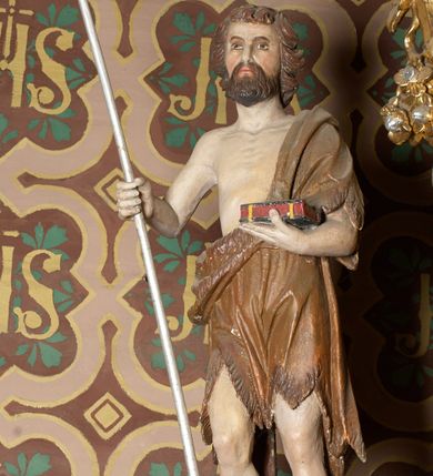 Zdjęcie nr 2: Rzeźba wolnostojąca, przedstawia św. Jana Chrzciciela, ustawiona na niskim, zielonym cokole na planie kwadratu. Święty ukazany frontalnie, w postawie stojącej z krzyżem o długim drzewcu w prawej dłoni oraz zamkniętą księgą w lewej. Twarz podłużna z długim i wąskim nosem, ze wzrokiem skierowanym w dal, okolona brązową, średniej długości brodą oraz krótkimi włosami, zasłaniającymi uszy.  Święty jest ubrany w szatę uszytą ze skóry zwierzęcej, odsłaniającą nagi tors i nogi poniżej kolan. Sylwetka szczupła. Polichromia w odsłoniętych partiach ciała naturalistyczna. 